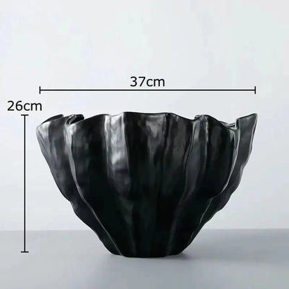 Black ceramic bowl with sculpted petal-like rim and glossy finish displayed alongside white porcelain jar with gold plating for living room decor