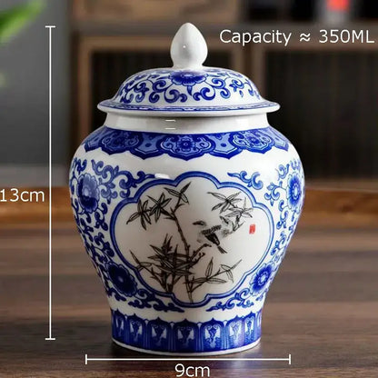 A white porcelain tea canister with blue and black floral and bird design and matching lid for kitchen storage
