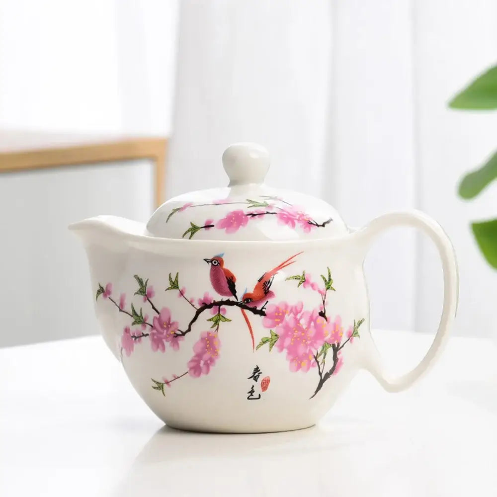 White porcelain tea pot set featuring delicate pink cherry blossoms and vibrant birds with elegant hand-painted details