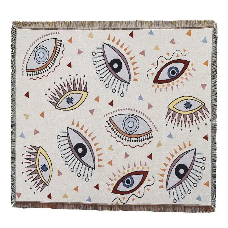 A cream-colored decorbites bohemian camping blanket with colorful stylized eyes pattern and fringed edges for living room decor