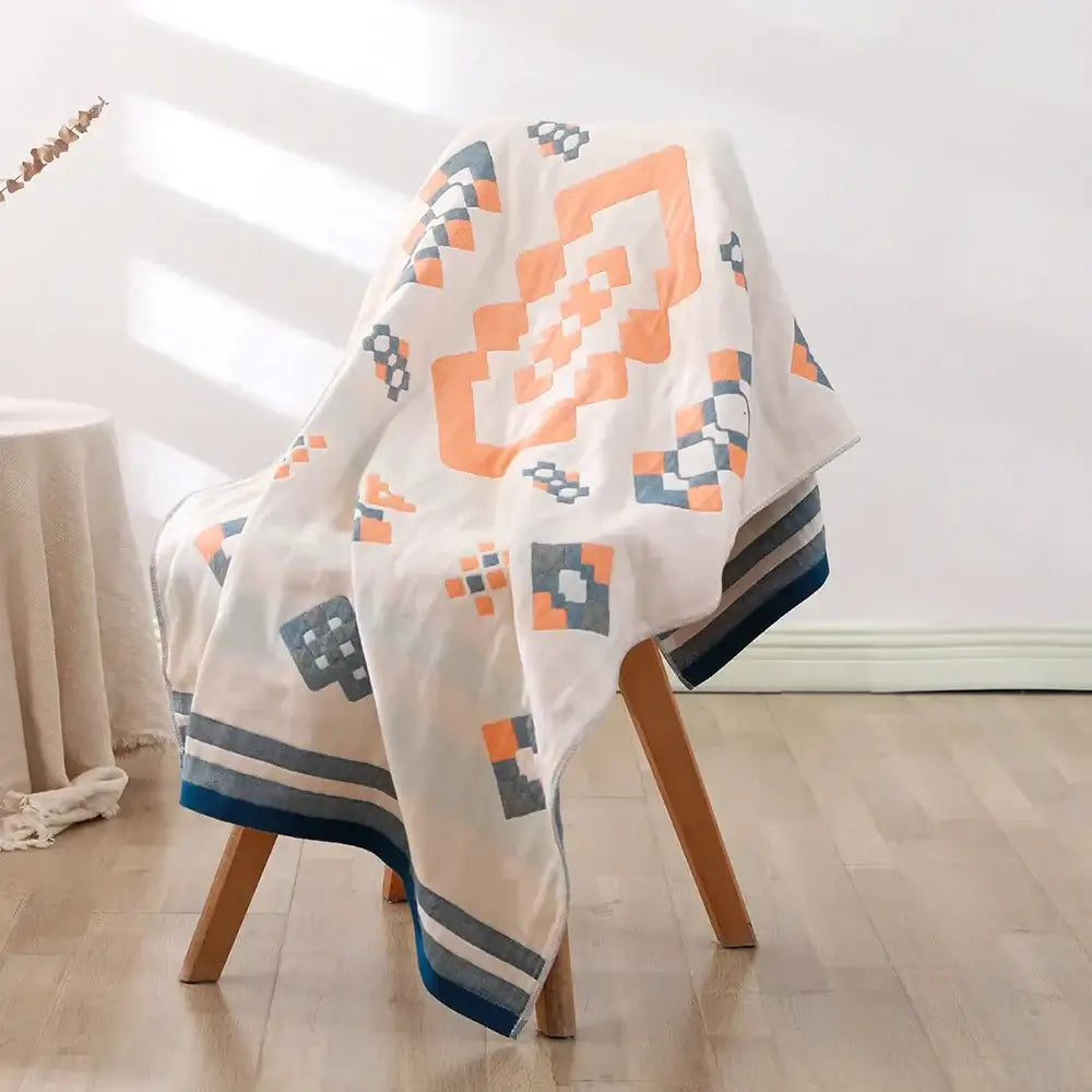A soft off-white bohemian floral cotton bath towel with orange and navy geometric pattern and striped trim by decorbites