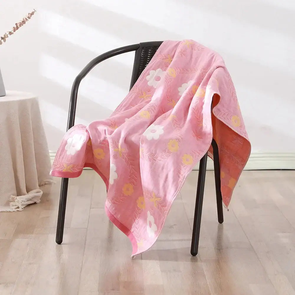 A soft pink bohemian floral cotton bath towel with white and yellow flowers draped over a black chair