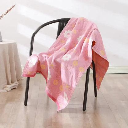 A soft pink bohemian floral cotton bath towel with white and yellow flowers draped over a black chair