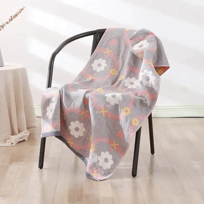 A soft gray decorbites bohemian floral cotton bath towel with white yellow and pink blossoms draped on a black chair