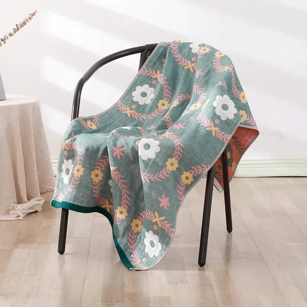A soft teal decorbites bohemian floral cotton bath towel with white yellow and pink flowers draped over a black chair