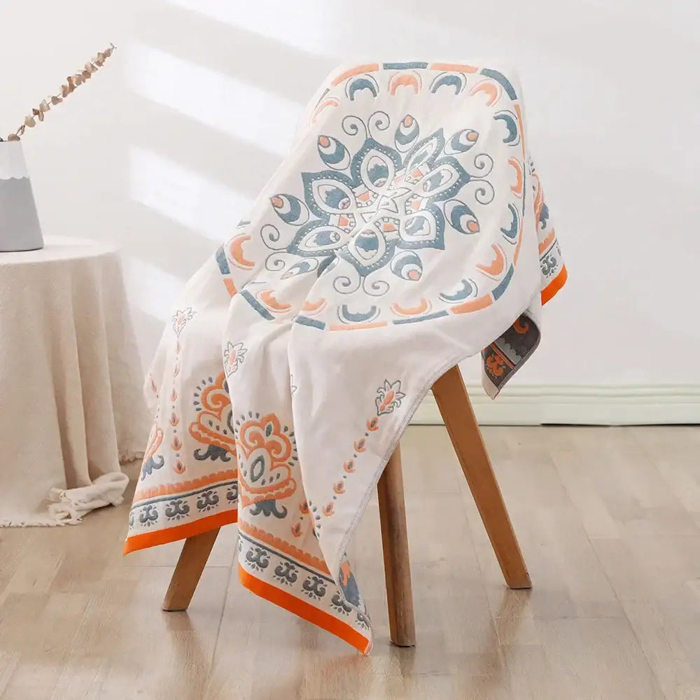 A decorbites bohemian floral cotton bath towel in white with vibrant orange and teal mandala pattern draped on a wooden chair