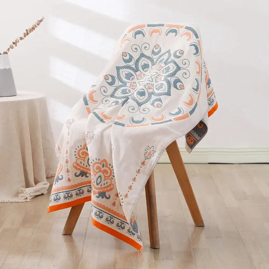 A decorbites bohemian floral cotton bath towel in white with vibrant orange and teal mandala pattern draped on a wooden chair