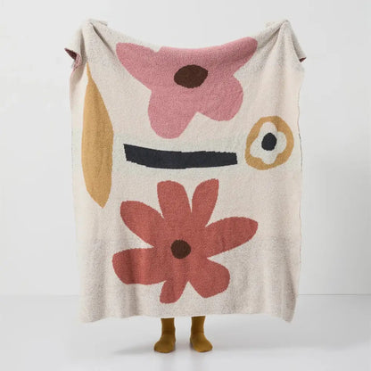 A soft cream-colored decorbites bohemian flower knitted throw blanket with abstract face and textured floral accents