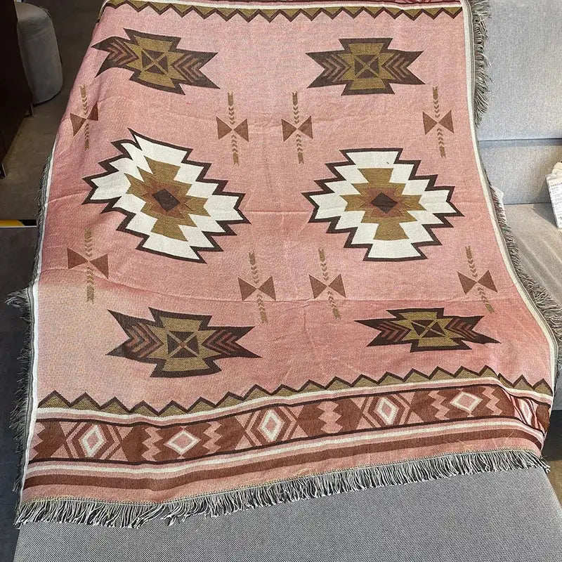 A soft pink decorbites bohemian knit throw blanket with bold white brown tan geometric patterns and fringed edges