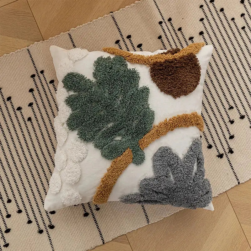 White bohemian loop plush cushion cover featuring textured green leaves brown acorn and gray foliage appliqué