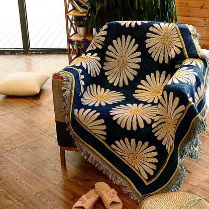 A cozy navy blue decorbites knitted cotton throw blanket with cream and gold daisy pattern and fringed edges