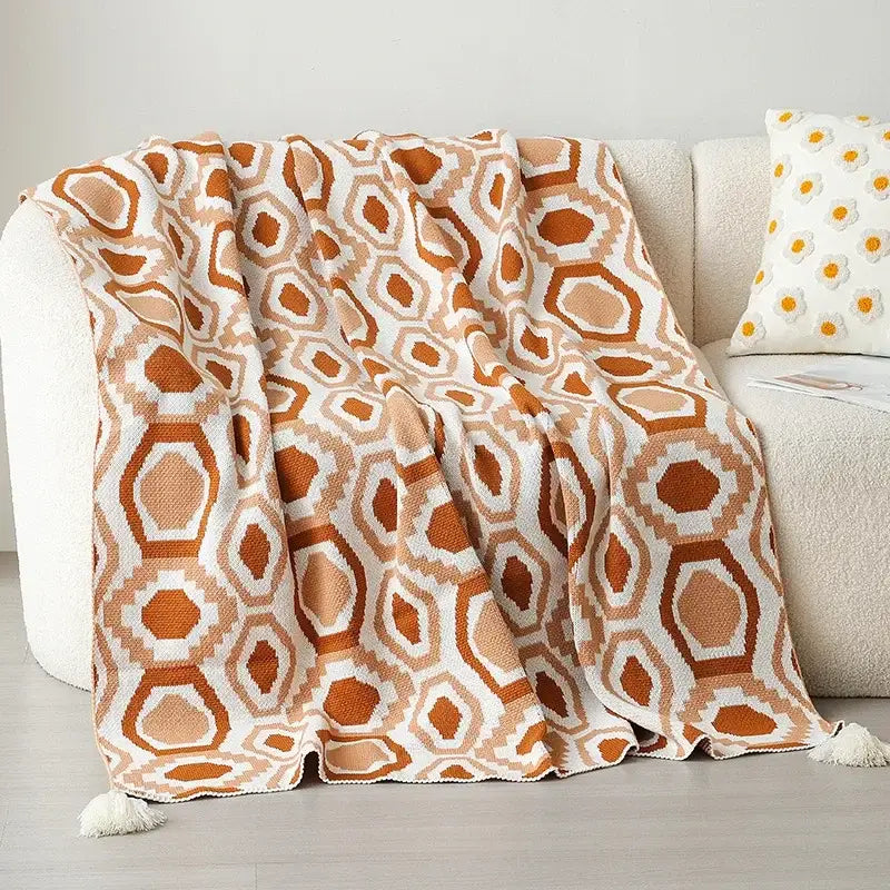 A cozy bohemian winter blanket in orange and white knitted with a geometric hexagonal pattern and tassels decorbites winter blanket
