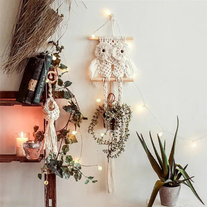 A cream-colored macrame plant hanger basket owl wall hanging with wooden dowel and tassels for boho decor