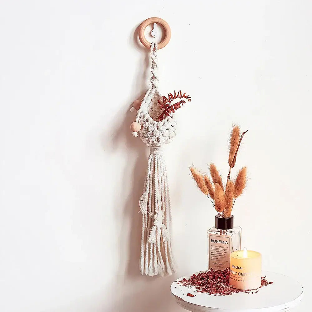 Cream-colored macrame plant hanger basket with wooden ring and tassels featuring dried foliage for living room decor
