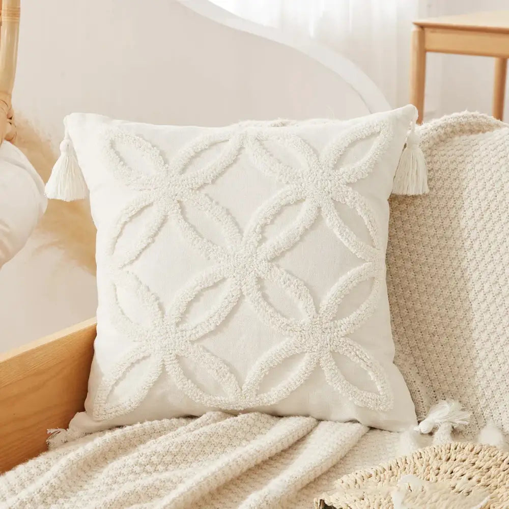 Cream-colored cushion cover with textured embroidered geometric pattern and tassels on each corner tufted tassel cushion cover