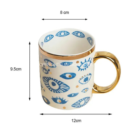 A white ceramic mug with gold rim and handle featuring blue eye patterns from decorbites bright eyes ceramic dinner collection