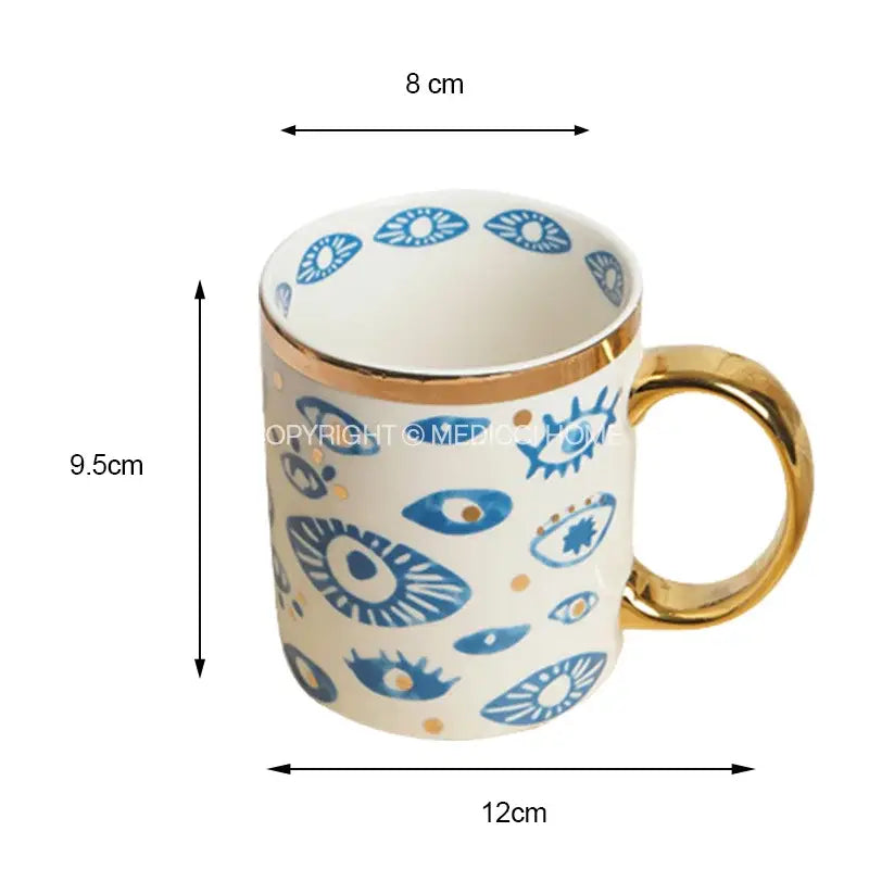 A white ceramic mug with gold rim and handle featuring blue eye patterns from decorbites bright eyes ceramic dinner collection