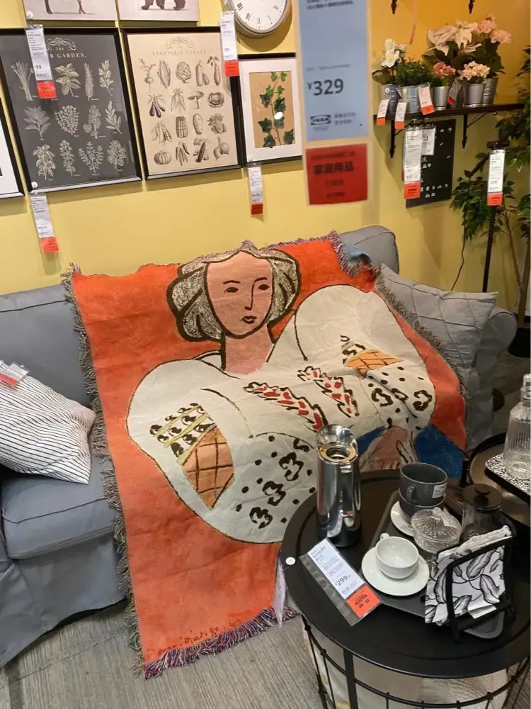 Orange boho chic throw blanket with blue leopard print and stylized woman illustration draped on gray sofa decorbites