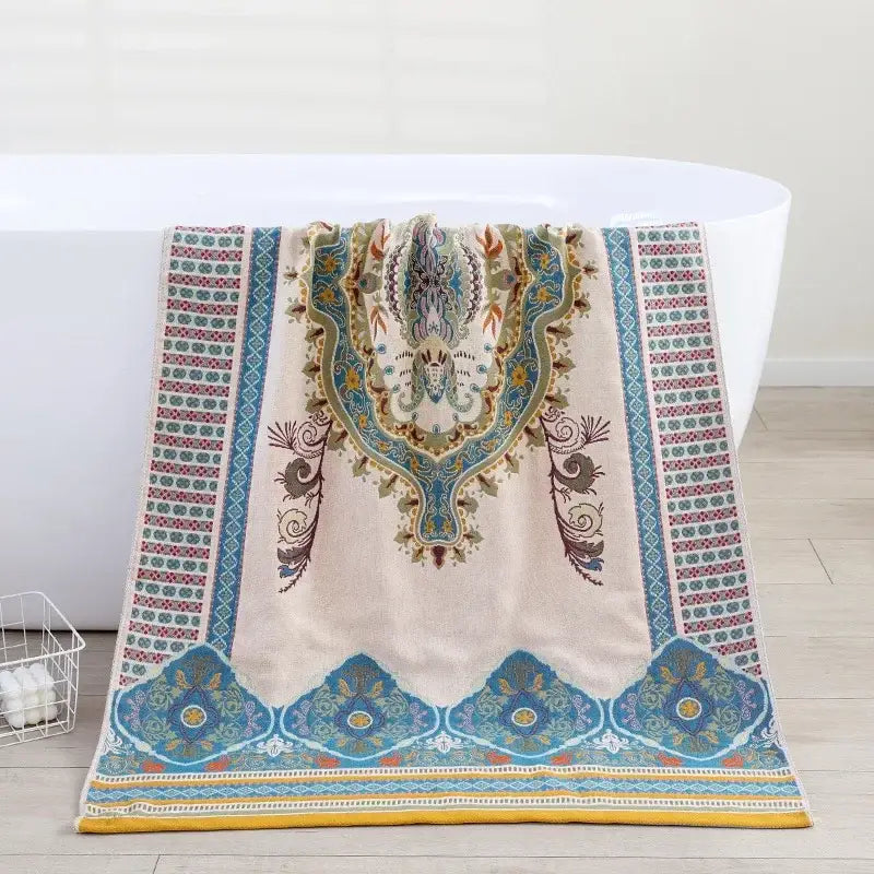A cream-colored decorbites boho cotton gauze bath towel with blue green and gold paisley patterns for bathroom wrap