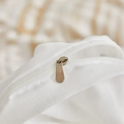 A sleek gold-toned zipper pull on soft white fabric of decorbites boho stripe pom pom duvet set