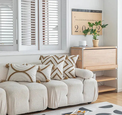 Cream-colored plush tufted sofa with beige and cream boho cushion covers featuring geometric tufted fringe pillows
