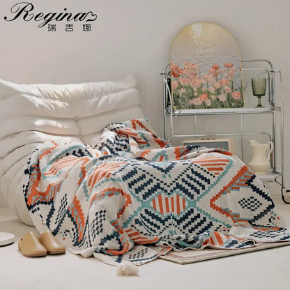 A cozy, hand-knitted throw blanket with a geometric pattern in orange, teal, and navy on a cream base.