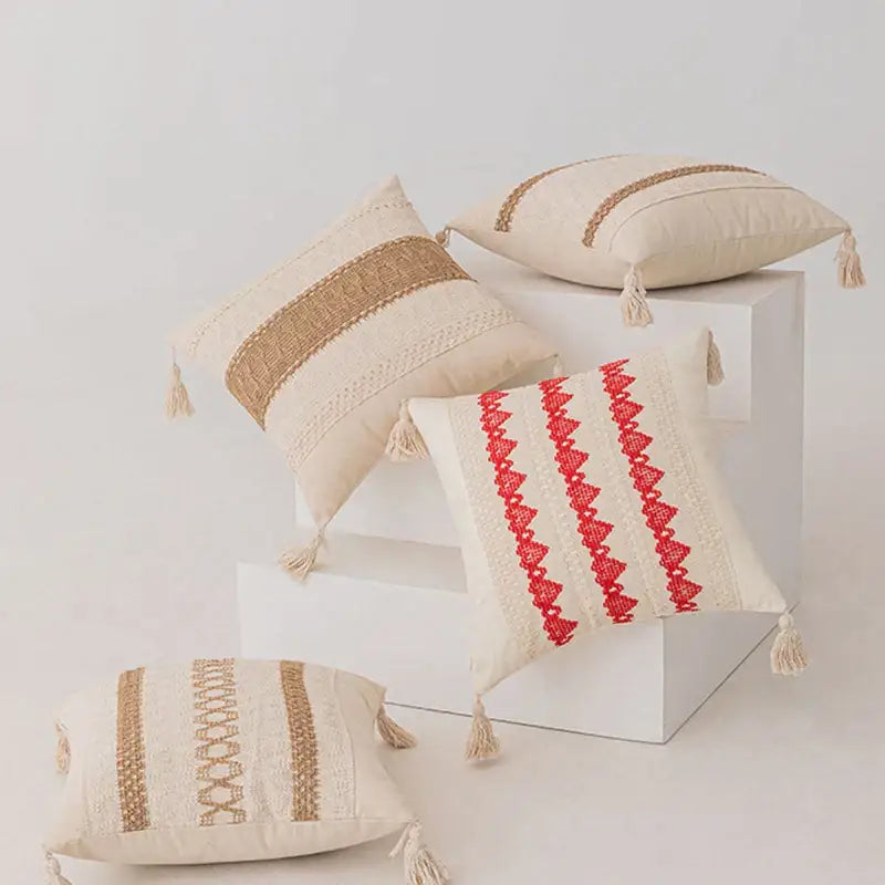 Beige and red embroidered throw pillows with woven stripes, tassels, and textured fabric.