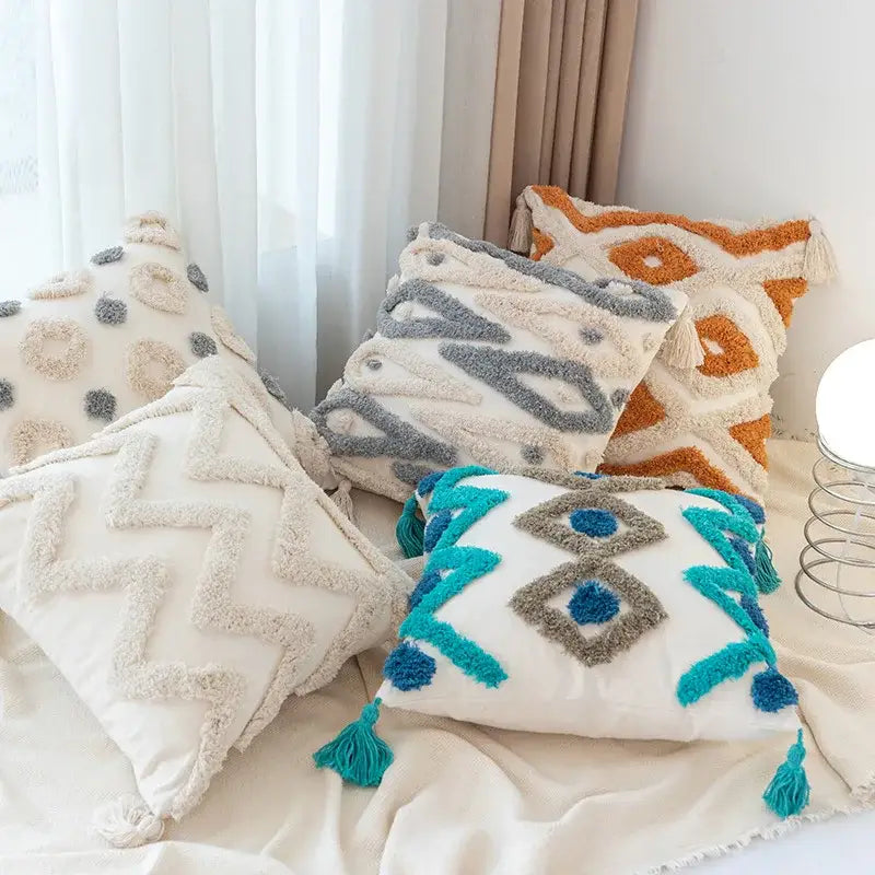 Set of four boho geometric tufted pillow covers in neutral and vibrant tones with tassel accents for living room decor