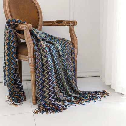 A vibrant multicolored boho knitted striped blanket with tassels draped over a wooden chair for living room decor
