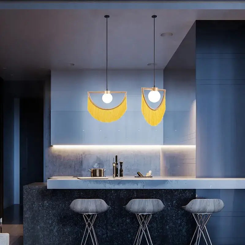 Two modern pendant lights with golden semi-circular frames and yellow fringe in a boho glass ball pendant light design for bedroom