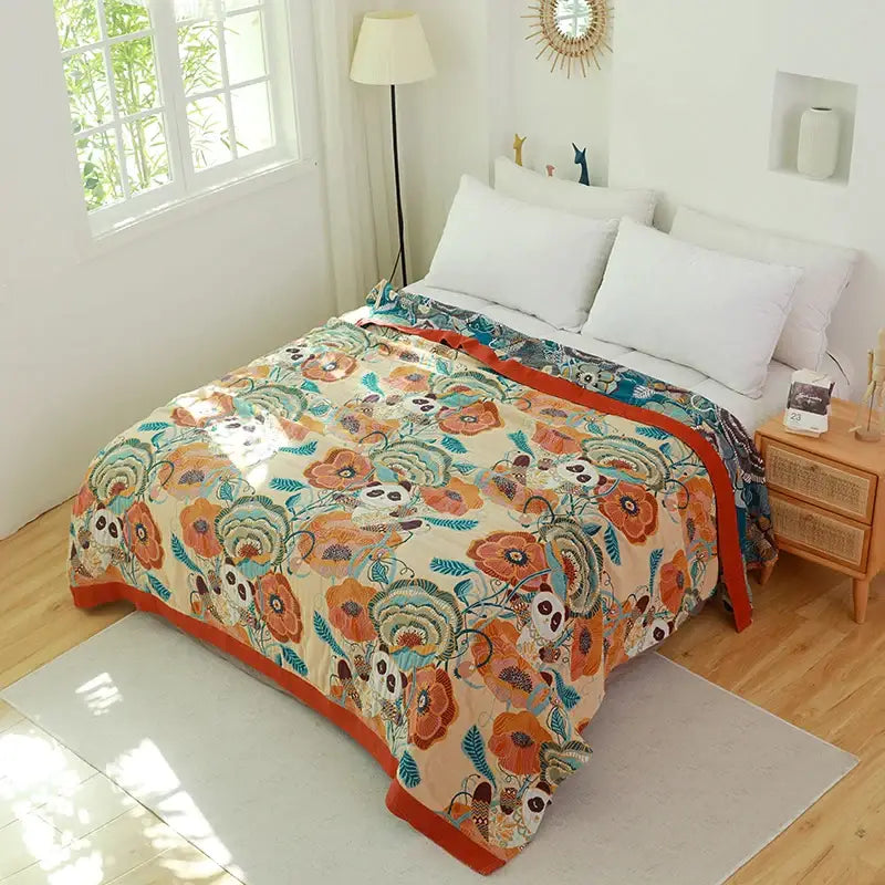 A cozy throw blanket with vibrant orange blossoms and panda faces on beige cotton boho manta with red borders