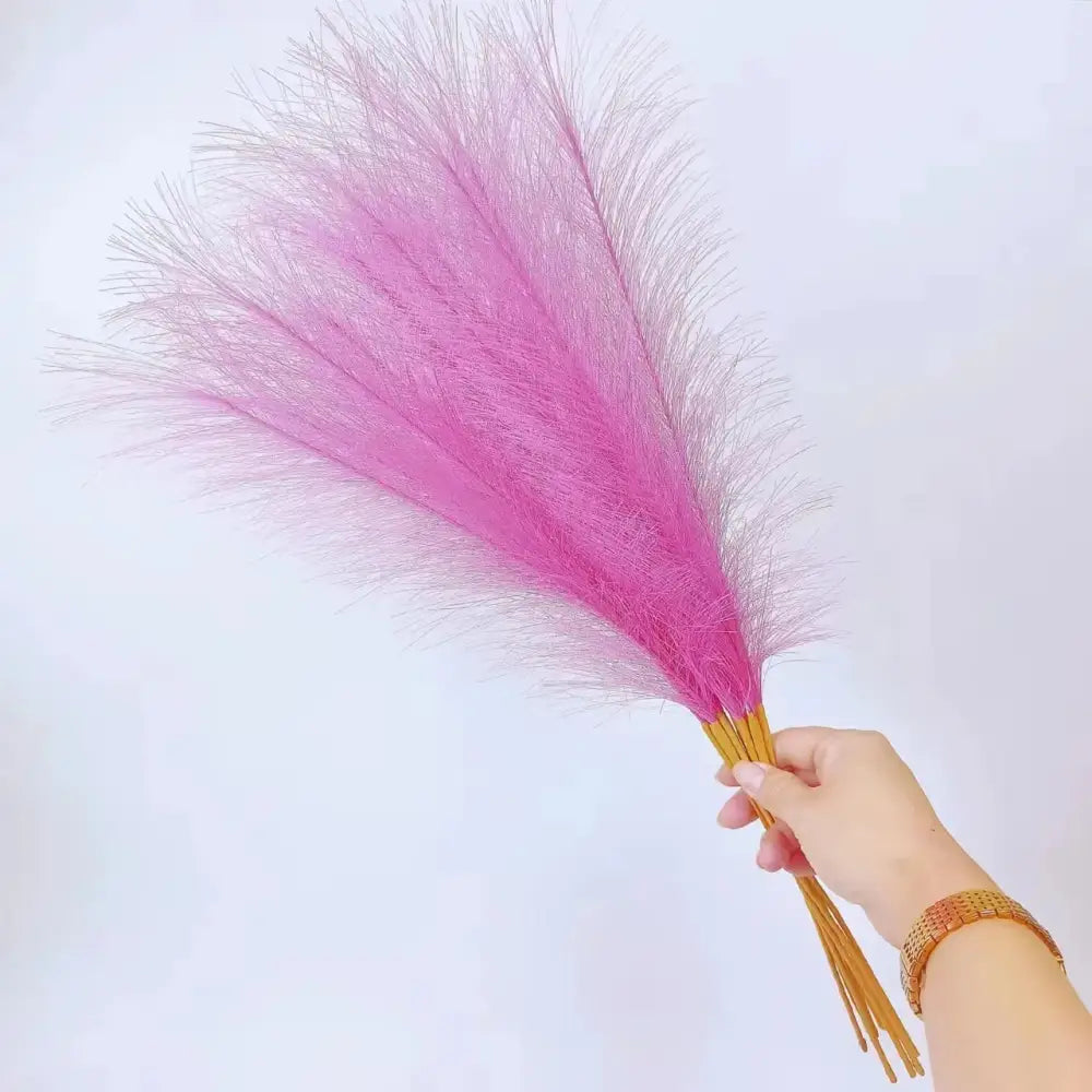 A hand holding a bundle of vibrant pink fluffy pampas grass with golden stems for boho living room decorbites decor