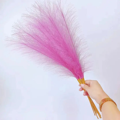 A hand holding a bundle of vibrant pink fluffy pampas grass with golden stems for boho living room decorbites decor
