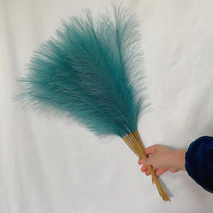 A hand holds teal fluffy pampas grass dusters with natural wooden handles for boho living room decorbites decor