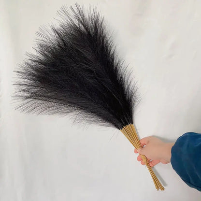 A hand holds black ostrich feathers with natural tan stems as part of boho fluffy pampas grass living room decor