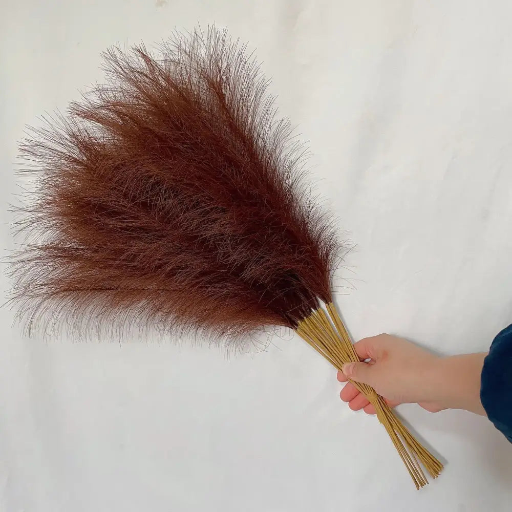 A hand holds a bundle of rust colored and beige fluffy pampas grass for boho living room decor by decorbites