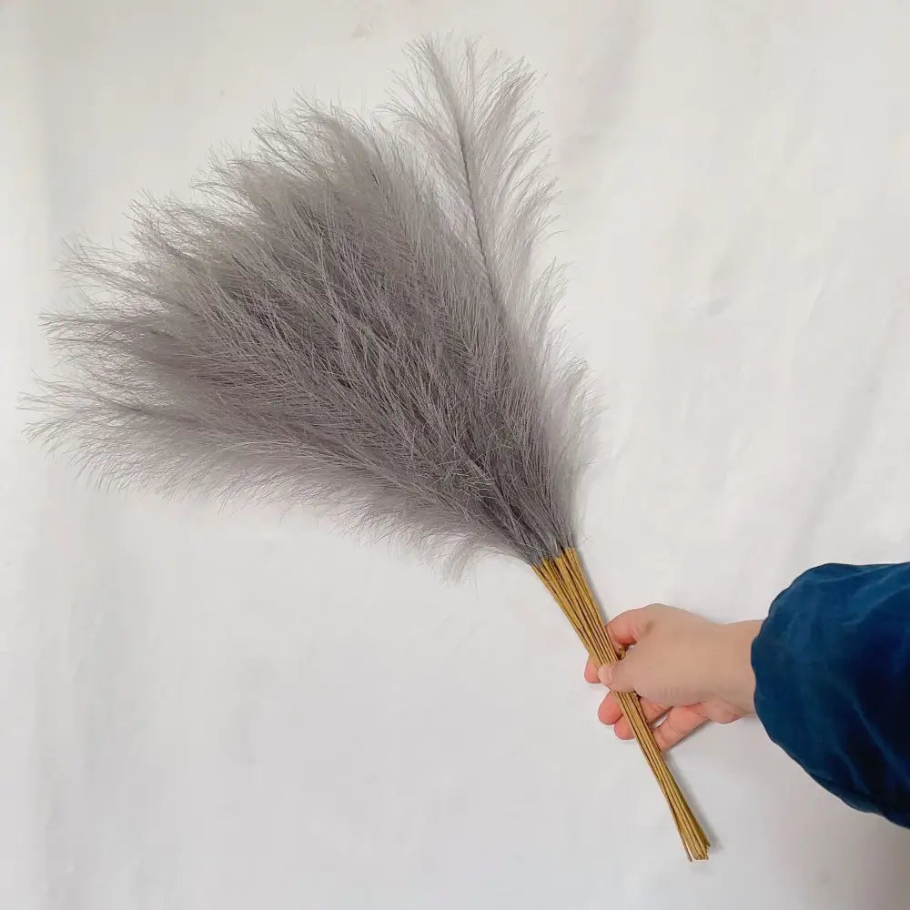 A soft gray feather duster with natural wooden sticks grip complements boho white beige fluffy pampas grass decorbites decor