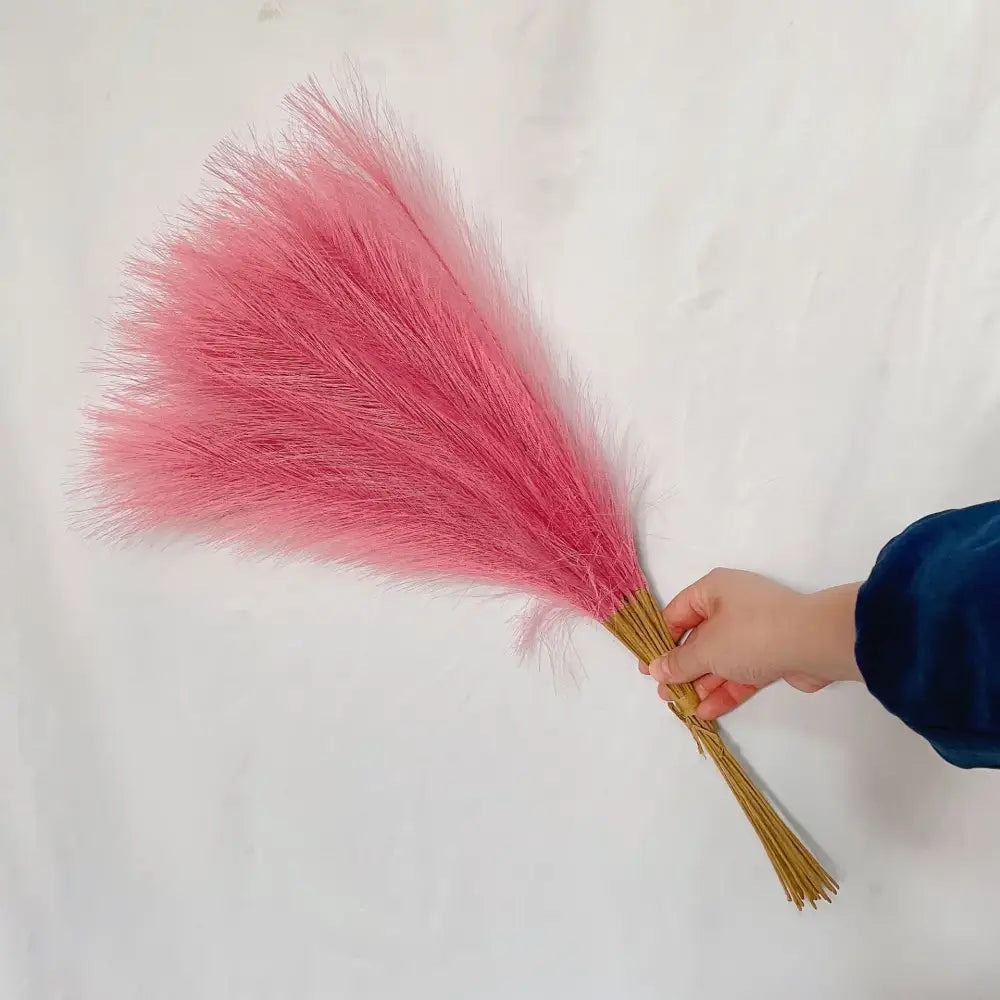 A hand holding vibrant pink fluffy pampas grass from decorbites boho white and beige living room decor