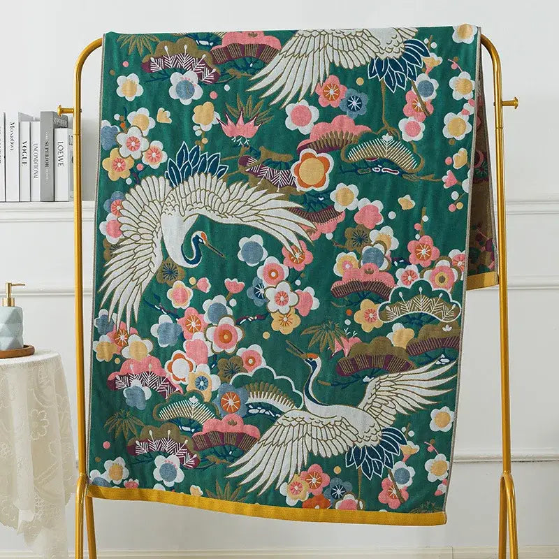 A vibrant green decorbites cotton gauze bath towel with white and blue cranes and pink orange floral pattern