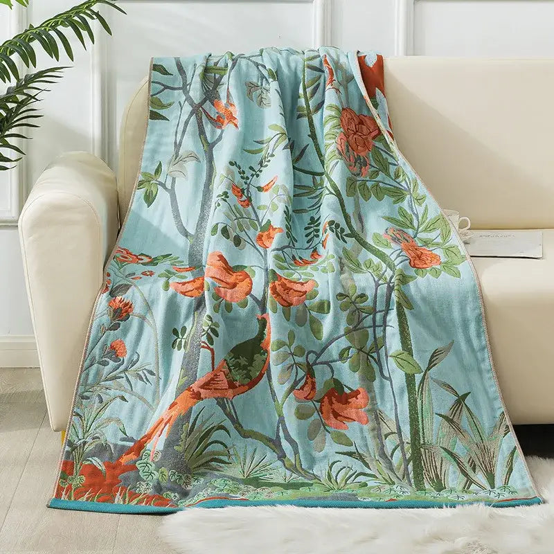 A soft light blue decorbites cotton gauze bath towel with vibrant orange birds and green foliage botanical design