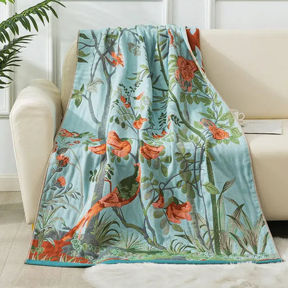 A soft light blue decorbites cotton gauze bath towel with vibrant orange birds and green foliage botanical design