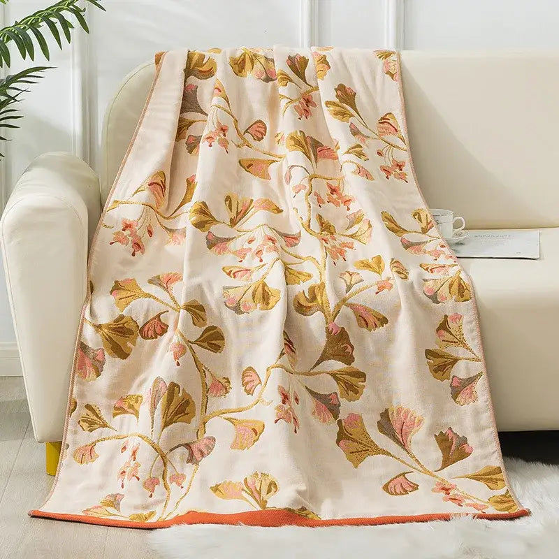 A cream-colored decorbites cotton gauze bath towel with embroidered golden and pink ginkgo leaves and orange trim