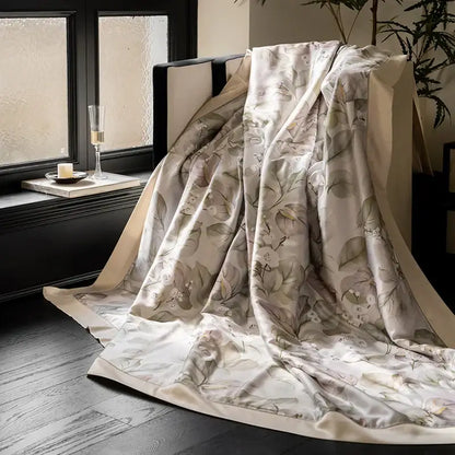 A cream silk throw blanket with botanical eucalyptus fiber flowers print draped over a dark chair for quilt set decorbites