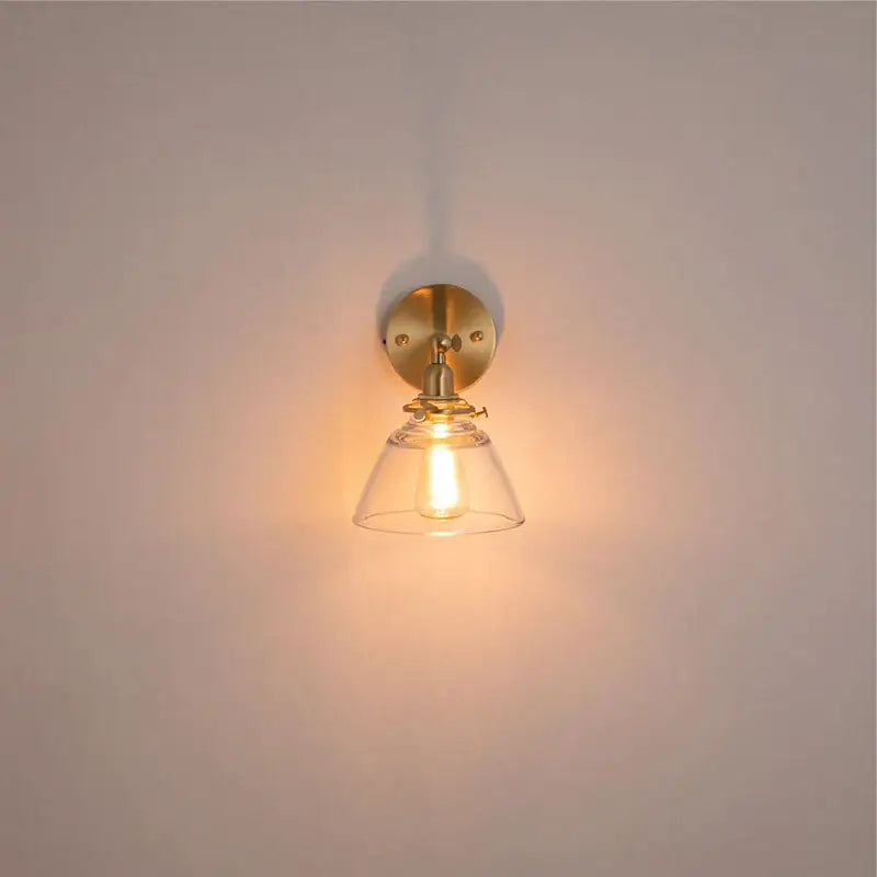 A warm-toned brass wall light with clear glass bell-shaped shade ideal for bedroom reading by decorbites clear glass