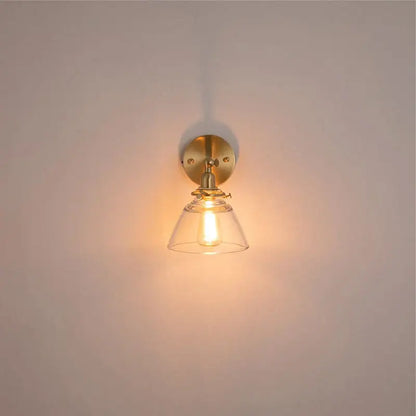 A warm-toned brass wall light with clear glass bell-shaped shade ideal for bedroom reading by decorbites clear glass