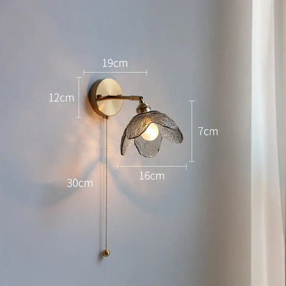 A brass flower gray glass led wall lamp with textured translucent shade and adjustable pull chain for bathroom use