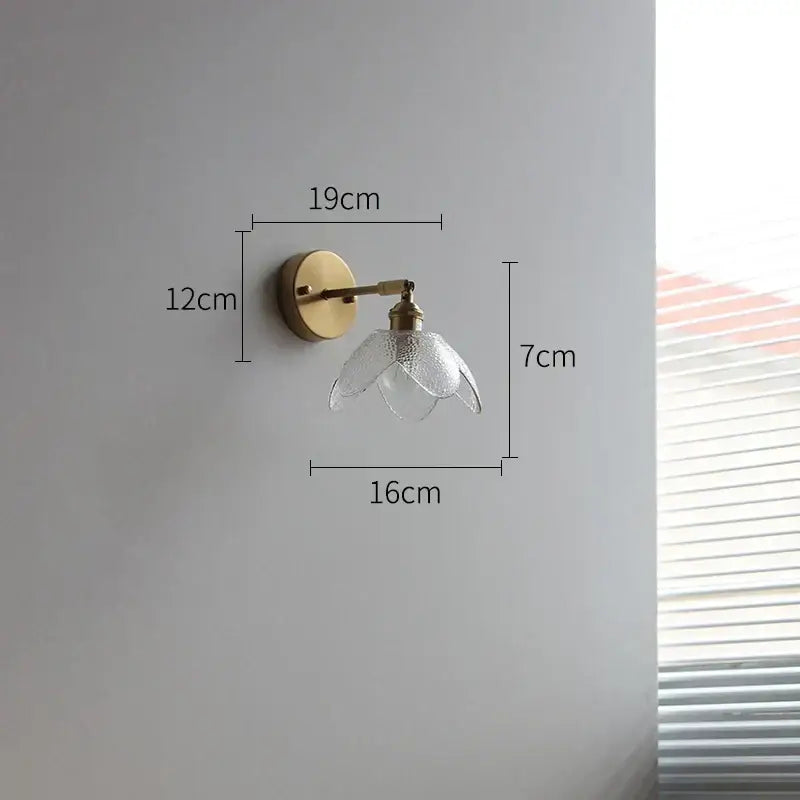 A delicate brass wall lamp with a gray clear glass led shade shaped like an open flower for bathroom use