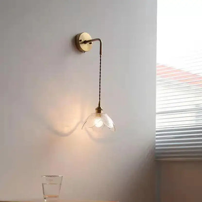 A delicate brass wall lamp with a twisted cord and gray petal-shaped glass led shade for bathroom use