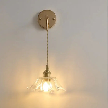 A delicate brass wall light with a clear petal-shaped glass shade adjustable led by decorbites for bedroom use