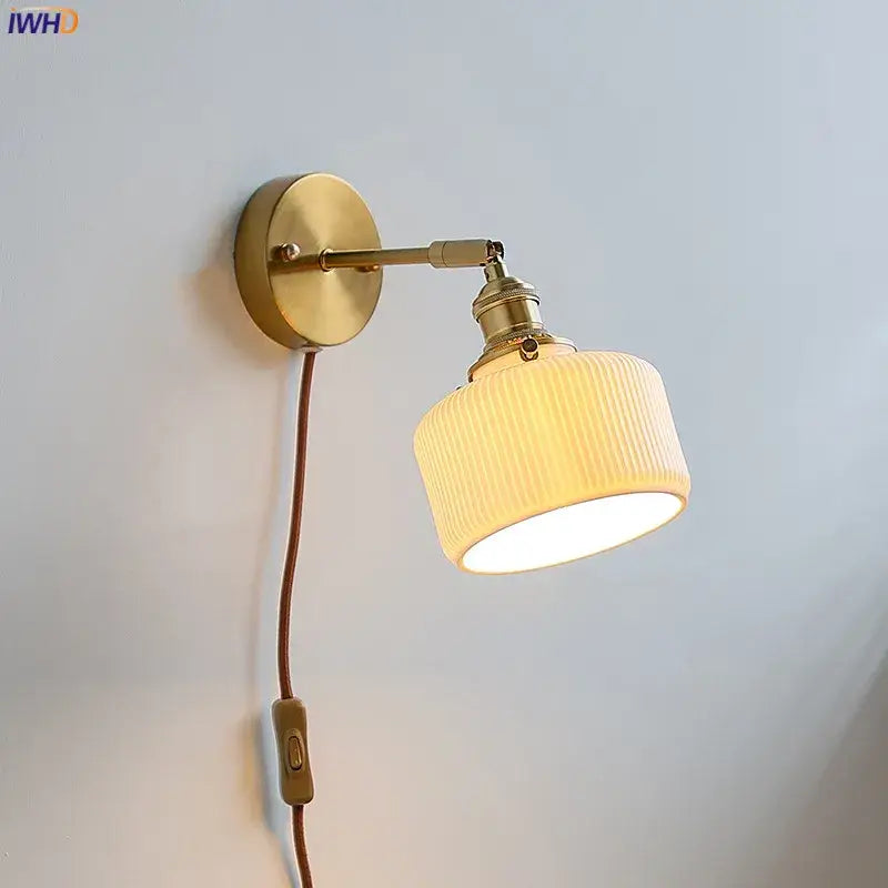 Brass ribbed decorbites ceramic wall sconce with iron arm, off-white ribbed ceramic shade, and brown cord for bedroom lighting